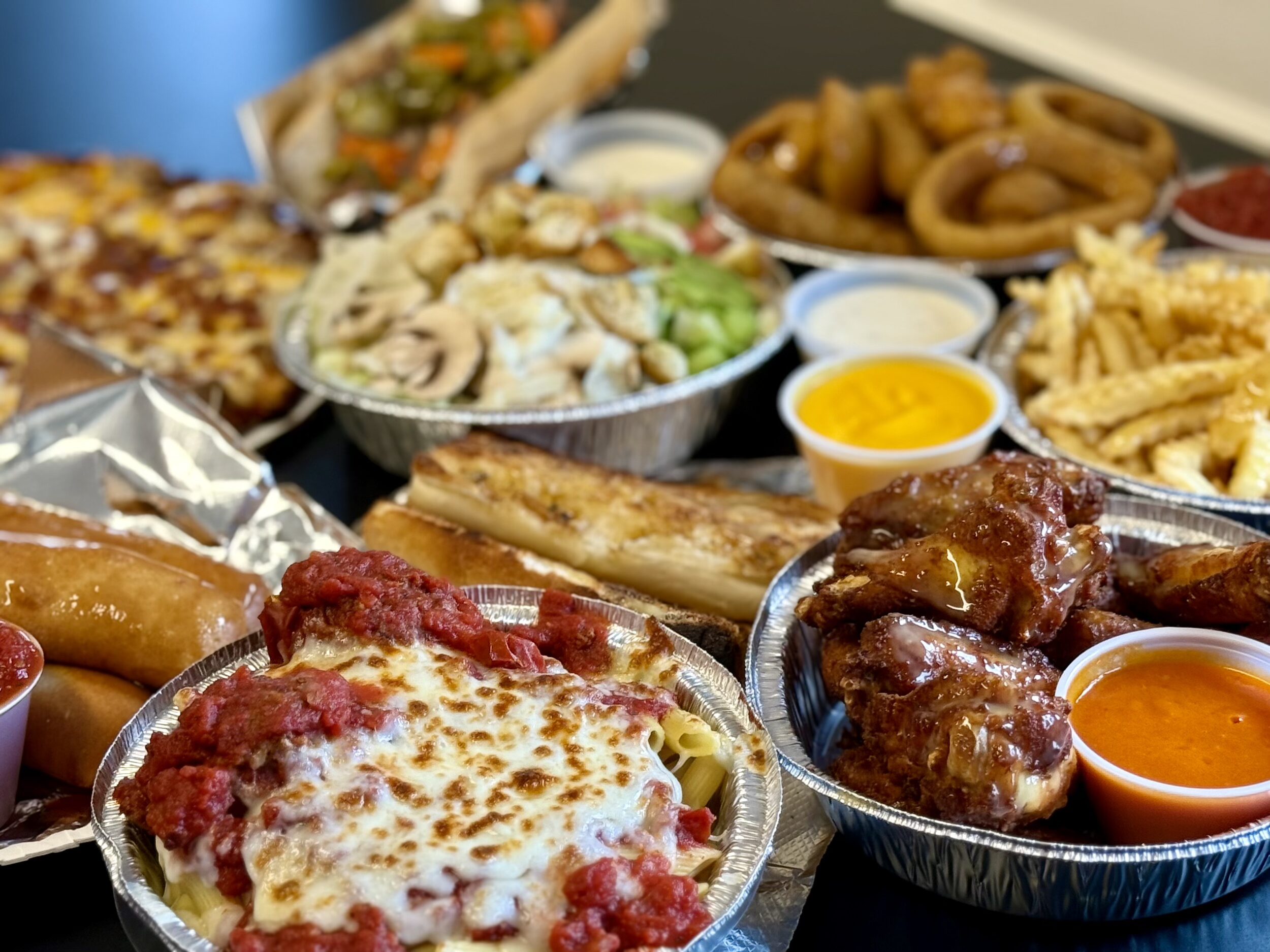 table full of various Antioch foods including pizza, pasta, wings, French fries, salad, and more!
